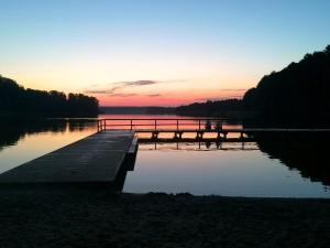 a dock on a lake with a sunset in the background at Dom w lesie in Łukta
