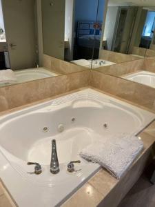 een groot wit bad in een badkamer met een spiegel bij Valley Vista Haven - Exquisite Condo Retreat with Jacuzzi - Top Floor Romance - Self-Check-in - Gourmet Kitchen - Heated Pool Paradise in Shanty Bay