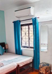 a room with two beds and a window with blue curtains at Baga Beach Paradise in Baga