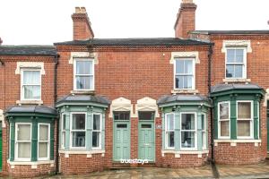 um antigo edifício de tijolos vermelhos com janelas verdes em NEW Balfour House by Truestays - 5 Bedroom House in Stoke-on-Trent em Etruria
