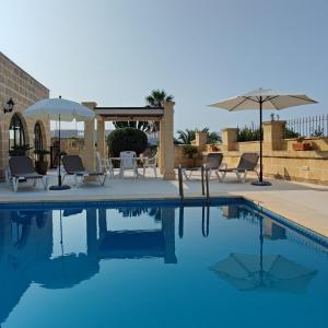 - une piscine avec des chaises, des tables et des parasols dans l'établissement Jenkins Holiday Farmhouse, à L-Għarb