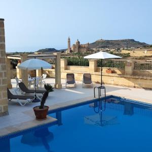 - une piscine sur le toit avec des chaises et des parasols dans l'établissement Jenkins Holiday Farmhouse, à L-Għarb