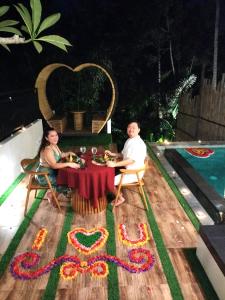 a man and woman sitting at a table next to a pool at Baruna Sari Villa yoga and reatret view jungle in Ubud