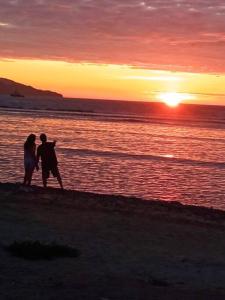 mężczyzna i kobieta spacerujący po plaży o zachodzie słońca w obiekcie Beach House SantaElena w mieście Pisco