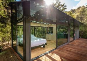a glass house with a bed on a wooden deck at Mākoha PurePod in Kerikeri