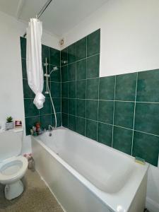baño con bañera, aseo y azulejos verdes en Cozy One Bed Apartment Near Purley Station en Purley
