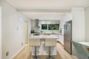 a white kitchen with a large island with two bar stools at Herne Bay 1BR Retreat in Auckland