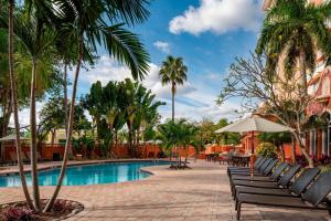 una piscina del complejo con sillas, mesas y palmeras en Sheraton Suites Fort Lauderdale at Cypress Creek, en Fort Lauderdale