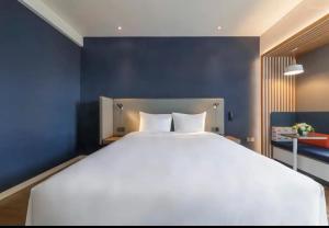 a large white bed in a room with a blue wall at Holiday Inn Express Qingdao Chengyang Central, an IHG Hotel in Qingdao