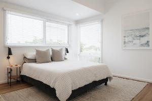 a white bedroom with a large bed and windows at Tassells Beach House in Safety Beach