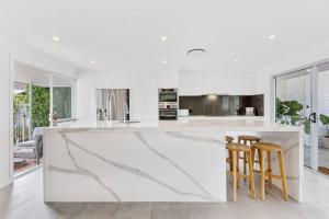 a white kitchen with a marble counter and stools at Broadbeach Waterfront home with pool in Gold Coast