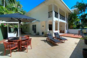 a patio with chairs and a table and an umbrella at Whispering Palms - Beachfront Port Douglas in Port Douglas