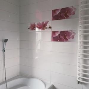 een badkamer met een bad en bloemen aan de muur bij Penthouse Noe in Kluczbork