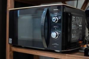 a black microwave oven sitting on a wooden shelf at シンプルでおしゃれなインテリアが光る4LDKの一軒家まるまる貸し切り！最大12名まで宿泊可能！ in Tokeshi