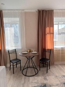 a dining room table with two chairs and a table and two windows at Центр. Аль-Фараби 100 in Kostanay