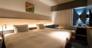 熊本市にあるグリッズプレミアムホテル熊本の白いベッドとデスクが備わるホテルルームです。