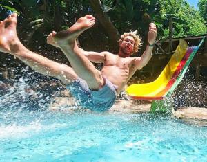 un homme tombant d'un toboggan dans une piscine dans l'établissement Mantis and Moon Backpackers and Surf Hostel, à Hibberdene