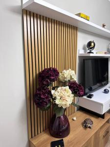 wazon kwiatów siedzący na stole obok telewizora w obiekcie Horta's home w Tiranie