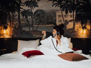 Hôtel Mercure Rochefort La Corderie Royale في روشفور: امرأة جالسة على سرير تتحدث على الهاتف الخلوي