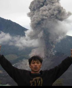 a man standing in front of a volcano with his arms outstretched at RINJANI EXPEDITION BASECAMP in Masbagik