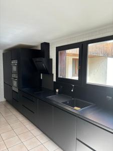 - une cuisine noire avec deux lavabos et deux fenêtres dans l'établissement Grande maison Proche Albertville, à La Bâthie