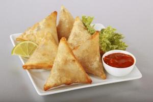 a plate of food with a pile of turnovers and salsa at Aerocity Hotel Zindal Plaza at Delhi Airport in New Delhi