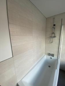 a white bath tub in a white tiled bathroom at Cozy, comfortable bedroom in a shared flat, within a walking distance of the train station in Wigan Town Centre in Wigan