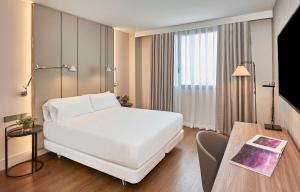 Cette chambre comprend un lit blanc et une table. dans l'établissement NH Alicante, à Alicante