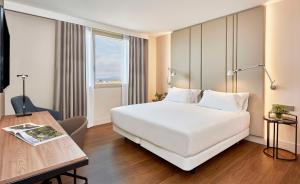 a hotel room with a large white bed and a desk at NH Alicante in Alicante