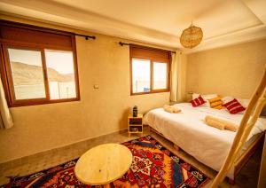 a bedroom with a bed and a table and two windows at The Moroccan Surf House in Imsouane