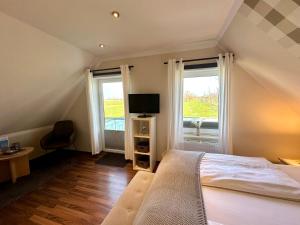 a bedroom with a bed and a tv and two windows at Landhotel Bauernstuben in Neuharlingersiel