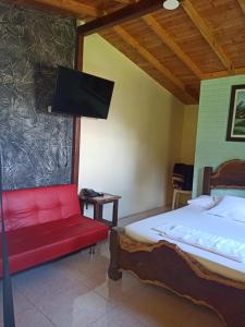 Habitación con cama, sofá rojo y TV. en Alojamiento Campestre Cabañas Mirador Ingrumá Riosucio Caldas, en Ruiosucio