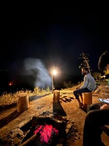 a man sitting next to a fire at night at Hide away valley in Kodaikānāl