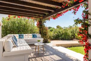 een patio met een witte bank onder een pergola met rode bloemen bij Villa Bini Uxuanne by Villa Plus in Binibeca