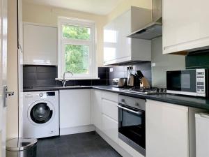 a white kitchen with a washing machine and a window at Modern And Vibrantly Designed Apartment in Motherwell