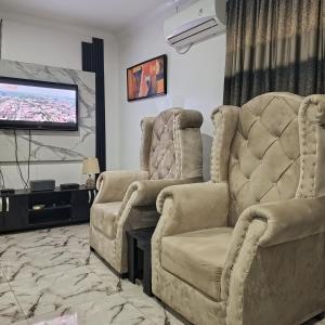 J Lounge في Ikorodu: غرفة معيشة مع كرسيين وتلفزيون بشاشة مسطحة