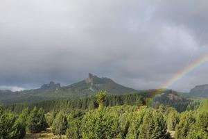 a rainbow over a forest of trees with a mountain at La Torre del Rio in Lago Meliquina +9 photos