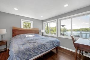 a bedroom with a bed and a desk and windows at Waterfront Sun-Drenched Hermit Lake Retreat! in Sanbornton