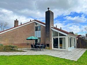 uma casa de tijolos com uma mesa e cadeiras e um guarda-sol em Vakantiewoning de Oeverzwaluw in hartje Drenthe em Zwiggelte