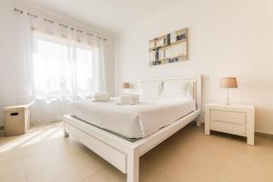a white bedroom with a white bed and a window at By the Beach in Praia d'el Rey in Óbidos