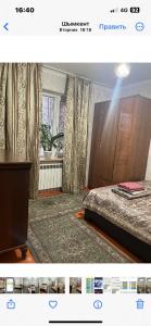 a bedroom with a bed and a table and a window at Квартира in Shymkent