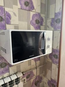a microwave oven on a wall with purple flowers at Квартира in Shymkent
