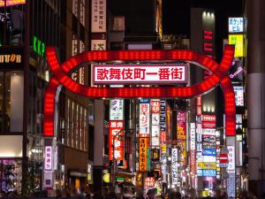 APA Hotel Higashi Shinjuku Kabukicho في طوكيو: شارع المدينة مزدحم ليلاً مع علامة حمراء كبيرة