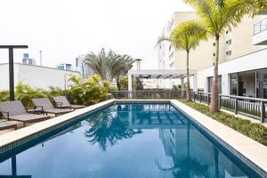 a swimming pool with chairs and palm trees next to a building at Apartamentos completos em Pinheiros a uma quadra da Faria Lima - HomeLike in Sao Paulo