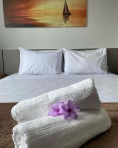 een wit bed met een handdoek met een paarse bloem erop bij Pousada Cantinho da Barra in Barra de São Miguel