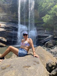 Bulatkohupitiya的住宿－Tropical river resort，坐在瀑布前的岩石上的女人
