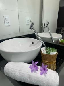 een badkamer met een witte wastafel en een handdoek met paarse bloemen bij Pousada Cantinho da Barra in Barra de São Miguel