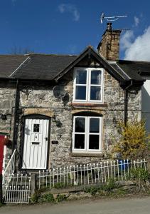 a stone house with a white fence in front of it at Annie’s Cottage in Llanrhaeadr-ym-Mochnant