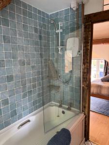 La salle de bains est pourvue de carrelage bleu, d'une douche et d'une baignoire. dans l'établissement Annie’s Cottage, à Llanrhaeadr-ym-Mochnant