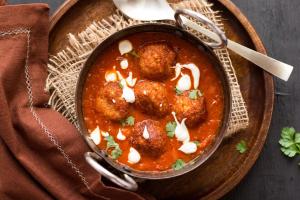a bowl of meatballs in a stew on a wooden plate at Hotel Airport Shine Inn in Shamshabad